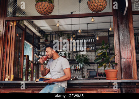 Happy young man sitting at cafe counter with a book and drinking coffee. Stylish caucasian male enjoying a cup of coffee at coff Stock Photo