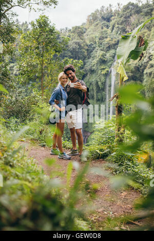 Loving young couple taking self portrait with their mobile phone. Man and woman in forest taking selfie. Stock Photo