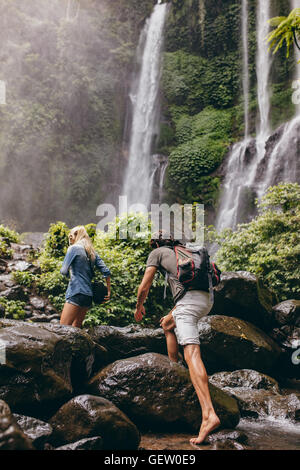 Couple crossing a stream together in the forest on a hike. Hiking man and man crossing a river. Climbing big rocks. Stock Photo