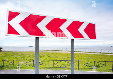 Dangerous turn. Red and white stripped arrow. Road sign in summer city Stock Photo