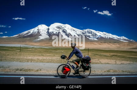 Single male cyclist on the bicycle cycling in front of the Muztagh Ata peak on the Karakorum Highway in China Stock Photo
