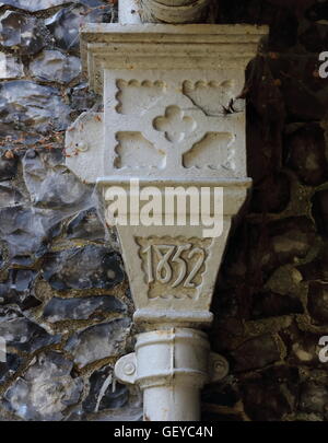 A dated cast iron water hopper from a gutter above, made of cast iron and painted white with ornate design set against flint. Stock Photo