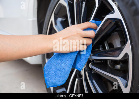 Hand with blue microfiber cloth cleaning car wheel. Stock Photo