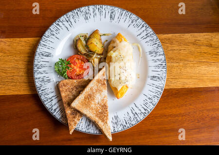 Omelet with potato, tomatoes parsley and feta cheese and bread in white plate on wooden table. Soft focus Stock Photo