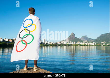 RIO DE JANEIRO - MARCH 27, 2016: Athlete stands draped in Olympic flag in front of Lagoa Rodrigo da Freitas Lagoon. Stock Photo