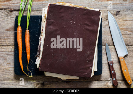 Vintage cook book with healthy recipes on wooden cutting board. Two young fresh carrots and two kitchen knifes on sides Stock Photo
