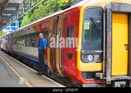 Guard standing by South West train for Lymington stopped at Brockenhurst railway train Station, New Forest, Hampshire UK in July Stock Photo