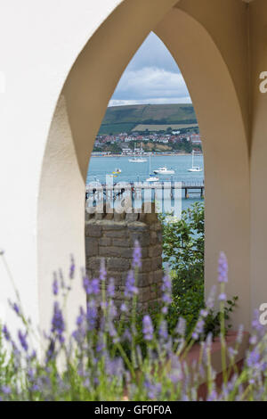 Looking through archway to Swanage pier with boats moored in the bay and Dorset coastline in July Stock Photo