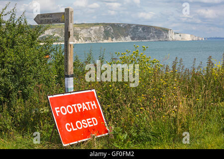 sign pointing the way to Swanage by Foreshore but footpath closed with Old Harry Rocks in the distance, Swanage in July Stock Photo