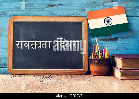 a chalkboard with the text Independence Day written in Hindi and a flag of India, on a rustic wooden surface, against a blue woo Stock Photo