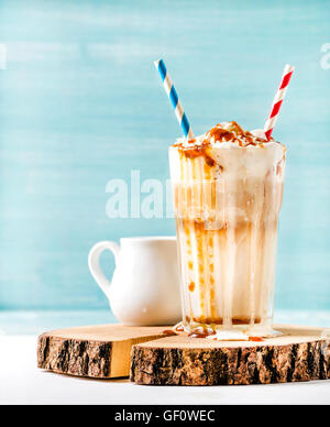 Latte macchiato with whipped cream and caramel sauce in tall glass on wooden board over blue painted wall background, copy space Stock Photo