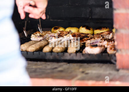 Photo of meet and potatoes on grill, shallow focus. A man hand moving the meat. Stock Photo