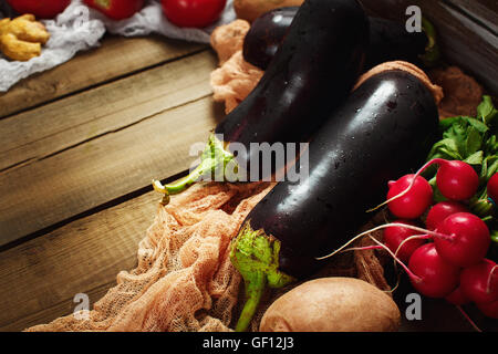 Great eggplants (aubergines) close-up in wooden box among fresh vegetables. Space for text, selective focus. Stock Photo