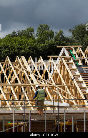 Roofers, workmen on piched roof;  New Build houses, with roofs, roof trusses, rafters or spars, Construction nearing completion in Buckshaw Village, near Chorley, Lancashire, UK Stock Photo