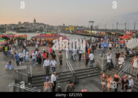 People walk on the Golden Horn waterfront by Galata bridge in Eminönü on a summer's evening.  The railings of Galata bridge can Stock Photo