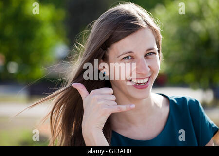 Portrait of attractive young woman on open air. Woman making a call me sign outdoors Stock Photo