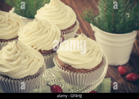 Homemade christmas cupcakes with cream cheese frosting on cake stand on wooden background with spruce twigs in ceramic pail Stock Photo