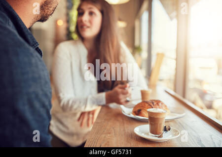 Cup of coffee and food on table with couple talking in background at cafe. Stock Photo