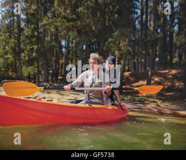 Portrait of happy mature couple having fun at the lake. Woman paddling kayak with man pushing from behind on a summer day. Stock Photo