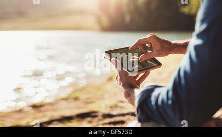 Close up portrait of male hands using digital tablet for navigation. Man sitting near a lake. Stock Photo
