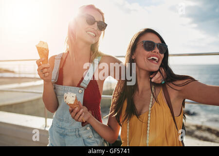 Shot of two female friends enjoying ice cream together on a summer's day. Close up of cheerful young women eating icecream at se