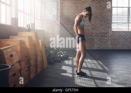 Full length indoor shot of determined young woman standing in gym. Tough female athlete at crossfit gym with exercise equipments Stock Photo