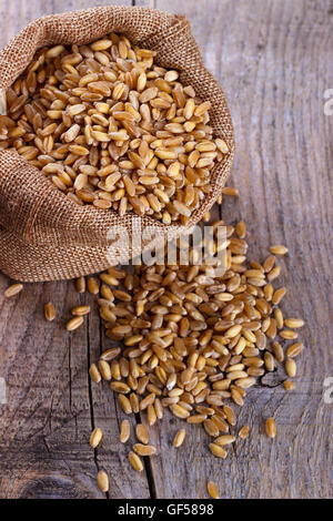Wheat in small burlap sack on rustic wooden background Stock Photo