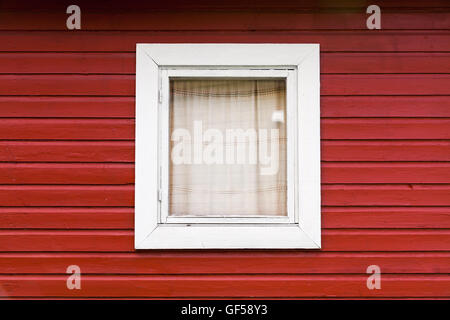 Red wooden wall with small window in white frame, typically Scandinavian living house architecture fragment Stock Photo