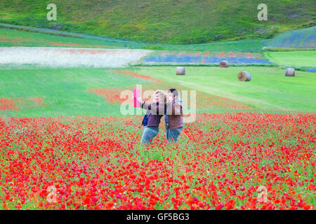 Castelluccio di Norcia, Italy - July 16, 2016: Two girlfriends taking a selfie in a blooming poppy field. In the background the Stock Photo