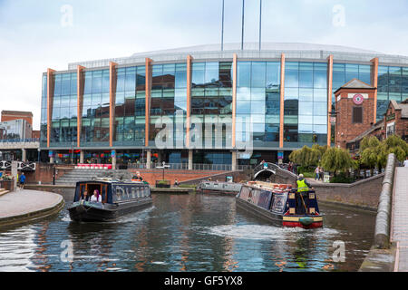 Narrowboats going along the canal in Brindleyplace in front of the National Indoor Arena (NIA). Stock Photo