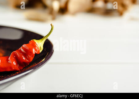 Closeup red pepper on brown dish over white wood. Horizontal image. Stock Photo