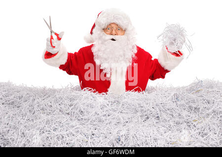 Studio shot of Santa Claus cutting paper with scissors and standing in a pile of shredded paper isolated on white background Stock Photo