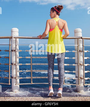 Look Good, Feel great! Seen from behind young athlete in fitness outfit looking into the distance at the embankment Stock Photo