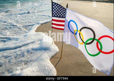 RIO DE JANEIRO - MARCH 24, 2016: Waves approach Olympic and American flags fluttering on the beach. Stock Photo