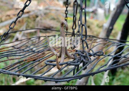 Rusty iron triple hook on grate hanging on chains. Shallow depth of field. Stock Photo