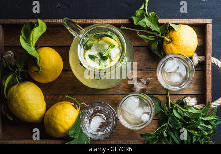 Jug and glasses with homemade lemonade, ice cubes on wooden tray, top view Stock Photo