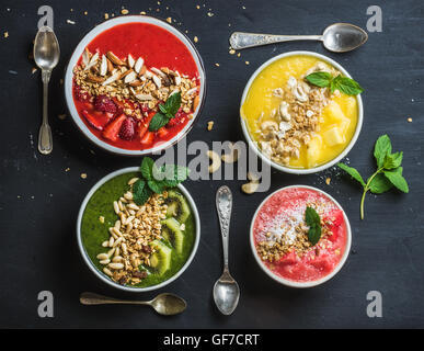 Healthy summer breakfast concept. Colorful fruit smoothie bowls with nuts, oat granola and mint leaves on black background. Red, yellow, green, pink. Top view Stock Photo