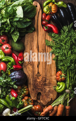 Fresh raw vegetable ingredients for healthy cooking or salad making on wooden background with rustic board in center, top view, copy space. Diet, vegetarian food concept Stock Photo