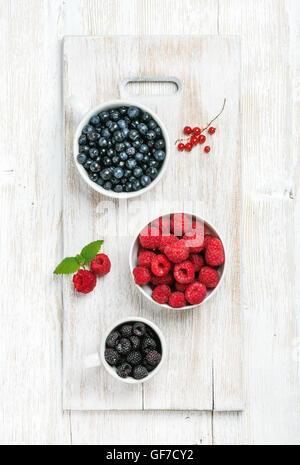 Summer garden berries in bowls on white painted wooden background Stock Photo
