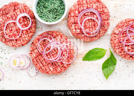 Raw ground beef meat cutlet for cooking burgers with onion rings and spices on white wooden background Stock Photo