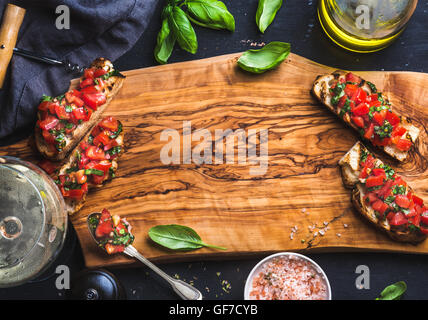 Tomato and basil bruschetta with glass of white wine on olive wooden board over black background Stock Photo