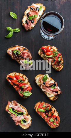 Brushetta set with glass of red wine. Small sandwiches on dark wooden background, top view Stock Photo