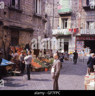 1960s, historical, a side street in Rome, Italy, showing local people and small stories and market stalls selling fresh fruit and vegetables. Clothes hanging on balconies to dry. Stock Photo