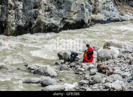 Kalash woman in a red embroidered dress washing by the river Stock Photo