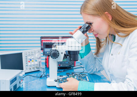 young researcher sits at a desk with a microscope used to look at electronics Stock Photo