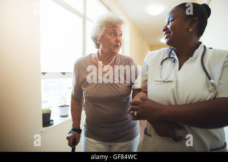 Portrait of healthcare worker and senior woman walking together. Nurse assisting senior female patient while walking in nursing Stock Photo