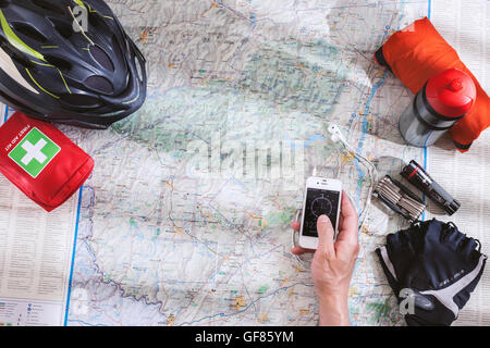 Bicycle accessories spread out on the map when planning a bike trip in the  mountains with compass app on smartphone in hand Stock Photo