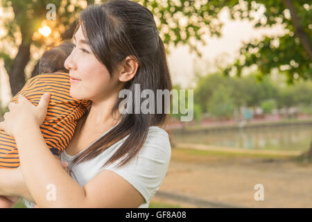 asian 2 months baby feeling happy and smiles with her mother in the garden and the sunset background