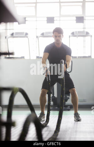 Young man exercising with battling rope at gym Stock Photo