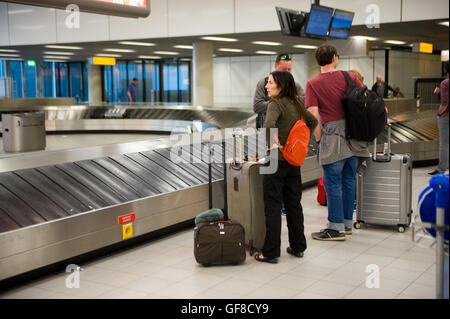 AMSTERDAM, THE NETHERLANDS - MAY 05, 2016: People are waiting on an airport at the luggage belt for their suitcases to arrive. Stock Photo
